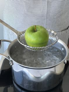 a green apple in a metal bowl on top of a stove