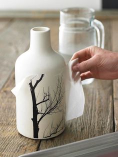 a hand is holding a piece of paper next to a vase with a tree on it