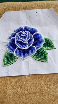 a piece of paper with bead work on it that has a blue rose in the center