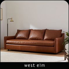 a brown leather couch sitting on top of a wooden floor next to a white wall