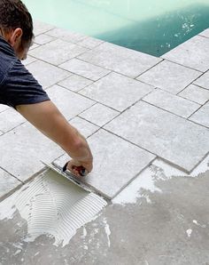 a man using a tiler on the ground next to a swimming pool with water