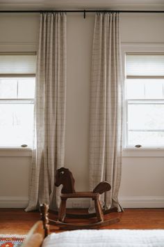 a rocking horse sits in front of two windows with drapes on the top and bottom