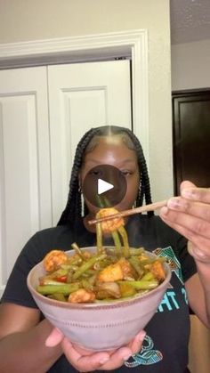 a woman holding a bowl filled with food and chopsticks in her hands,