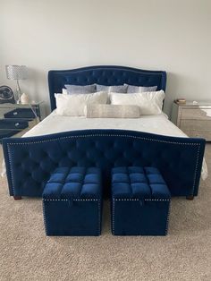 a bed with blue velvet upholstered headboard and foot stools on carpeted floor