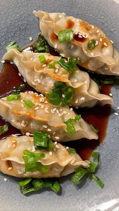 some dumplings are on a plate with sauce and green onions in them, topped with sesame seeds