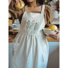 a woman in an apron is holding a bowl and oranges