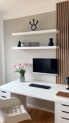 a white desk with a computer monitor, keyboard and flowers in a vase on it