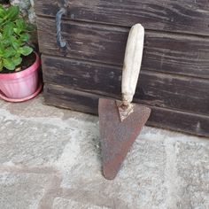 an old shovel leaning against a wooden wall next to a potted plant with a piece of bread sticking out of it