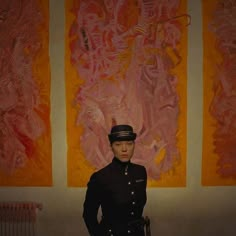 a man in uniform standing next to two paintings on the wall and holding his hands on his hips