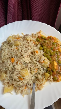 a white plate topped with rice and vegetables next to a fork on a table top