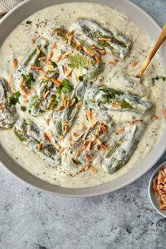 a bowl filled with broccoli covered in cream sauce next to some nuts on the side