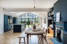 a dining room table and chairs in front of an open kitchen with blue walls, wood flooring and large windows