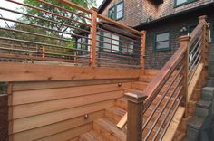 a wooden deck with railing and handrails next to a house in the woods