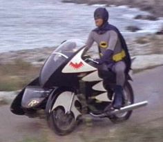 a man riding on the back of a motorcycle down a road next to the ocean