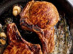 two pork chops cooking in a skillet with potatoes and herbs on the side