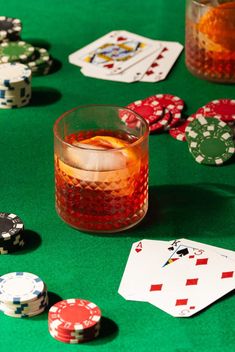 some cards and dices on a green table with drinks in glasses next to them