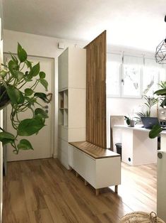 a living room with wooden floors and white furniture in the center, plants on either side of the door