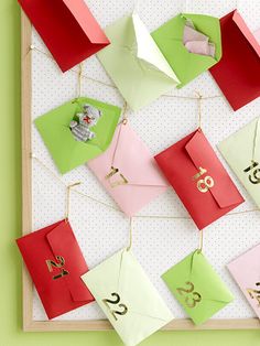 an assortment of different colored envelopes hanging from strings on a white board against a green wall