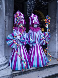 two clowns dressed in purple and blue holding candy canes on their heads, standing next to each other