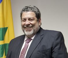 a man in a suit and tie standing next to two yellow and green flags, smiling at the camera