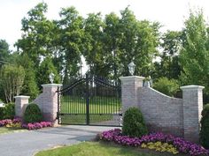 an iron gate and brick wall in front of a driveway with purple flowers on the side