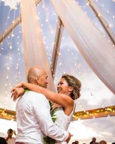 a bride and groom dance together under a canopy with string lights at their wedding reception