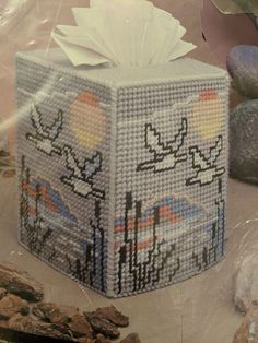 a tissue box made out of plastic beads with birds and flowers on it sitting next to rocks