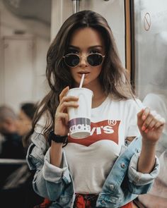 a woman wearing sunglasses and holding a drink in her hand while sitting on a train