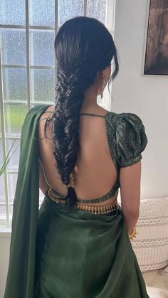 a woman with long hair wearing a green sari and gold jewelry, standing in front of a window