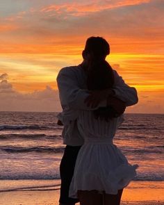 a man and woman hugging on the beach at sunset