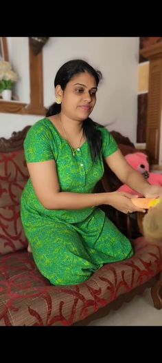 a woman in green dress sitting on couch holding a pink and yellow frisbee