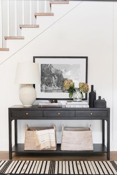 a black console table with two white vases on top and a framed photograph above it