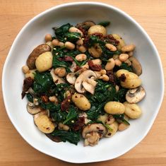 a white bowl filled with spinach, mushrooms and other vegetables on top of a wooden table