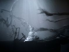 a man sitting on top of a piano under water with long hair flying around him