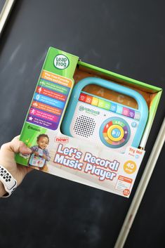 a child's hand holding up a toy radio with its box open and instructions on how to use it