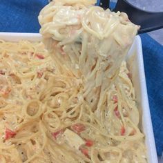 a spoon full of noodles and sauce being lifted from a casserole dish on a blue towel