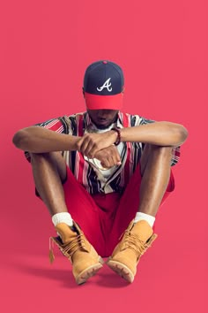 a man sitting on the ground with his legs crossed wearing a hat and red pants