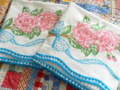 two embroidered napkins with flowers on them sitting on a quilted tablecloth covered in colorful fabrics