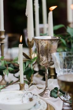 a table topped with candles and plates covered in greenery