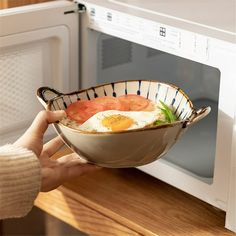 a person is holding a bowl with food in front of an open microwave oven door