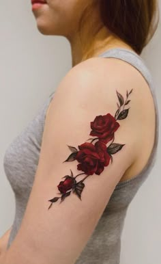 a woman's arm with red roses tattooed on the shoulder and behind her is a grey tank top