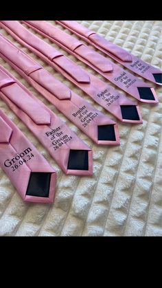 five pink ties with black labels on them sitting on a white sheeted bed spread