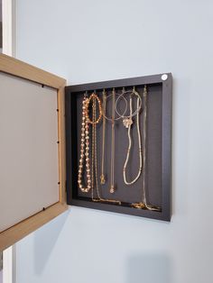 an open wooden box with jewelry hanging from it's sides on a white wall