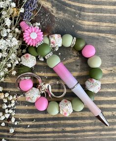 a pink and green beaded keychain with flowers on it next to a pen