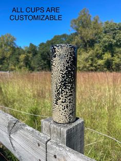 a tall metal vase sitting on top of a wooden fence in front of some grass