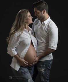 a man and woman standing next to each other in front of a black background holding their stomach