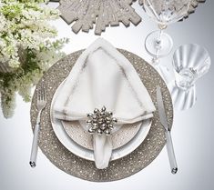 the table is set with silver and white plates, silver napkins, and flowers