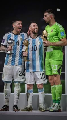 three soccer players standing next to each other holding trophies