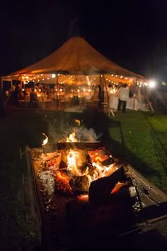 an open fire pit in the middle of a field at night with people standing around it