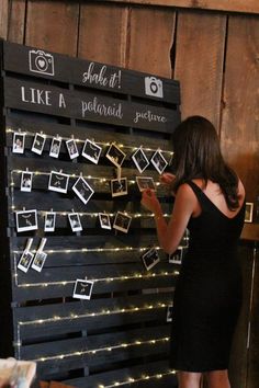 a woman standing in front of a black board with pictures on it and lights strung from the sides